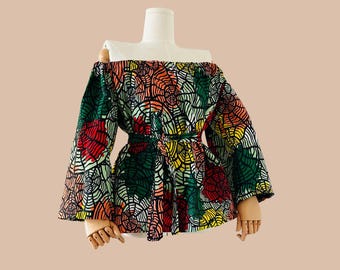 May include: Off-the-shoulder blouse with long sleeves and a tie waist. The blouse is made of a colorful fabric with a geometric pattern in shades of red, green, yellow, and pink.