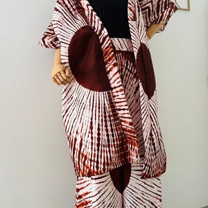 Puede incluir: Un conjunto de tres piezas sobre un maniquí. El conjunto incluye una camiseta sin mangas negra, pantalones de pernera ancha y una chaqueta tipo kimono de manga corta. La tela presenta un estampado de rayos de sol blanco y marrón. El maniquí está sobre un fondo blanco.