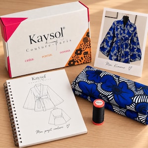 Op de afbeelding: Een naaipakket met een witte doos met de tekst Kaysol Couture-Paris, een spiraalblok met een kimonoschets, gevouwen blauw-witte bloemenstof, een klosje zwart garen en een fotokaart met het opschrift Mon Kimono en een hartje.