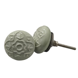 May include: Two light green ceramic cabinet knobs with a floral design. The knobs have a rounded shape and are attached to a metal base with a threaded screw. The knobs are set against a white background.