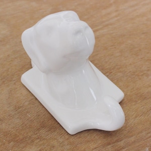 May include: White ceramic dog hook with a raised head and tail. The hook is attached to a white ceramic base.