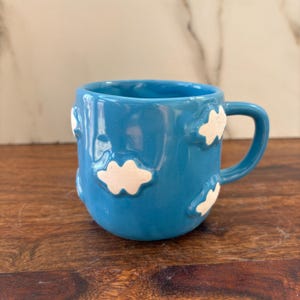 May include: A blue ceramic mug with white cloud-shaped details. The mug has a rounded shape and a handle.