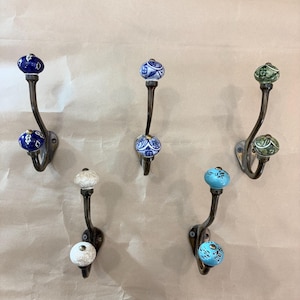 以下が含まれることがあります： 装飾的な壁掛けフックのコレクションで、装飾的なセラミックノブが付いています。 フックは濃い色の金属製で、青、白、緑など、ノブにはさまざまな色と模様があります。 各フックは、ダブルまたはシングルノブのデザインです。