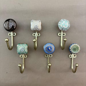 May include: A collection of decorative wall hooks with brass-colored metal bases. The ceramic hook heads feature various patterns in colors like black, white, blue, and green. The hooks are designed for hanging items.