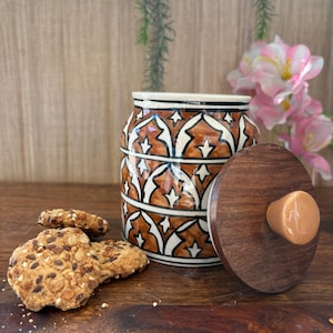 Op de afbeelding: Een keramische koekjespot met een bruin en wit geometrisch patroon en een houten deksel met een knop. De pot is gevuld met koekjes.