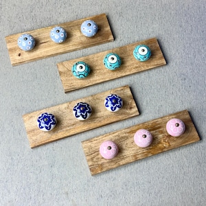 May include: A selection of decorative cabinet knobs in various colours and designs. The knobs are mounted on small wooden planks. The knobs feature floral and patterned designs in blue, turquoise, and pink. The knobs are made of ceramic.