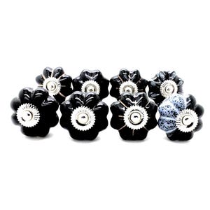 May include: A set of ten black and white ceramic cabinet knobs with a flower design. The knobs have a silver center and are perfect for adding a touch of elegance to any room.