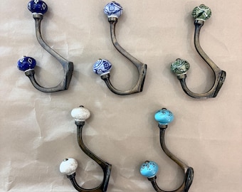 May include: Set of five decorative metal wall hooks with ceramic knobs. The hooks have a curved design and are in a bronze finish. The ceramic knobs are in various colors, including blue, white, and green, with patterned designs.