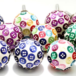 Op de afbeelding: Een verzameling van 10 ronde, kleurrijke kastknoppen met een knoopmotief. De knoppen zijn gemaakt van hout en hebben een witte achtergrond met verschillende gekleurde knoppen.