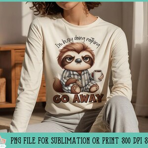 May include: A white long-sleeved shirt with a cartoon sloth wearing a blue and white striped shirt and holding a cup of coffee. The text "I'm busy doing nothing" and "GO AWAY" is printed on the shirt.