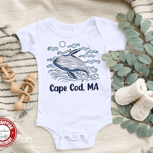 May include: White baby onesie with a blue whale illustration and the text "Cape Cod, MA".