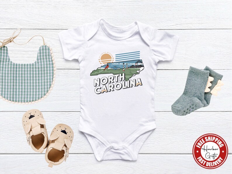 May include: White baby bodysuit with a graphic of the state of North Carolina, a lighthouse, and the text "North Carolina".