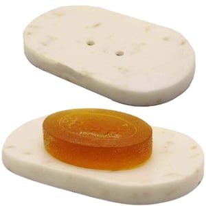 May include: A white oval soap dish with two drainage holes. A round orange soap bar is sitting on the dish.