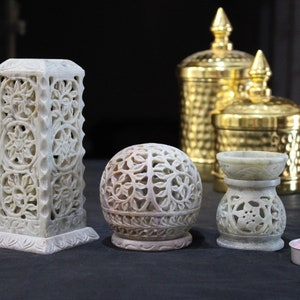 May include: A set of five decorative incense holders made of carved white stone. The holders are in various shapes, including a sphere, a cylinder, and a cone. There is also a small tealight candle holder.