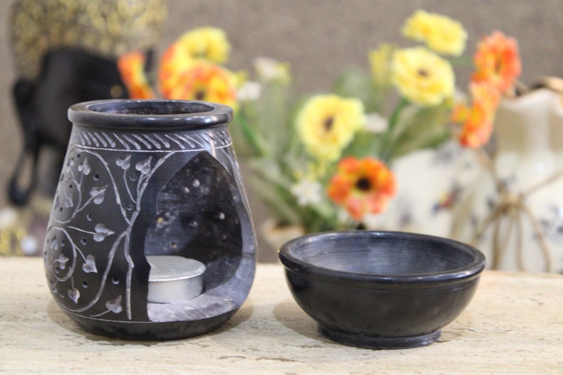 Puede incluir: Un quemador de aceite de piedra negra con un intrincado dise&ntilde;o tallado y una peque&ntilde;a vela blanca en su interior. El quemador se combina con un cuenco de piedra negra a juego.