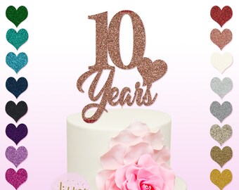 May include: Rose gold glitter cake topper with the number 10 and the word "Years" with a small heart. The topper is on a white cake with a pink rose.
