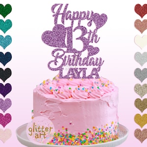 Pu&ograve; includere: Topper per torta di glitter viola con il testo "Happy 13th Birthday Layla". Il topper presenta un grande numero 13 e due cuori. Il topper &egrave; posto su una torta glassata rosa con codette colorate.
