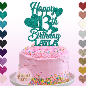 Pu&ograve; includere: Un topper per torta di glitter turchese con il testo "Happy 13th Birthday LAYLA". Il topper &egrave; su una torta rosa con codette colorate.