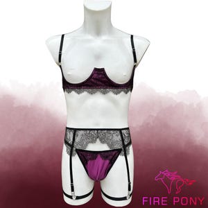 May include: A three-piece lingerie set in shades of purple and black, displayed on a mannequin. The set includes a bra with lace trim, a garter belt, and a matching thong. The bra and thong are a deep purple color, while the garter belt has black lace.