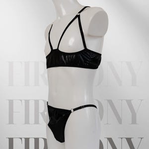 May include: Black jockstrap and cupless top set. The top has a criss-cross strap design and the jockstrap has a single strap. The set is made of a shiny, wet-look fabric. "Jockstrap + Cupless top" and "SIZE XS-3XL" are printed on the image.