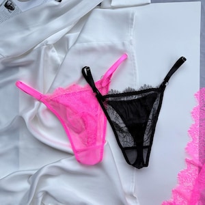 May include: Two pairs of lingerie. One is bright pink with matching straps and lace trim. The other is black with black straps and lace trim. Both are displayed on a white surface with white fabric.