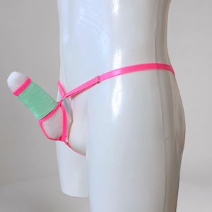 Könnte beinhalten: Ein neonpinker Tanga mit einer hellgrünen Stofftasche und pinkfarbenem Saum. Das Kleidungsstück wird auf einem weißen Schaufensterpuppen-Torso präsentiert und verfügt über dünne, verstellbare Träger, die mit der vorderen Tasche verbunden sind.