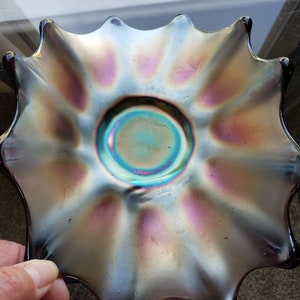 May include: An iridescent glass bowl with a scalloped edge and a central circle. The bowl has a dark blue, purple, and green colour scheme.