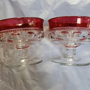 Könnte beinhalten: Zwei klare Glasschalen mit rotem Rand und einem strukturierten Muster. Die Schalen stehen auf einer weißen Oberfläche.