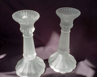 May include: Two frosted glass candle holders with a fluted design. The candle holders are white and have a scalloped base.