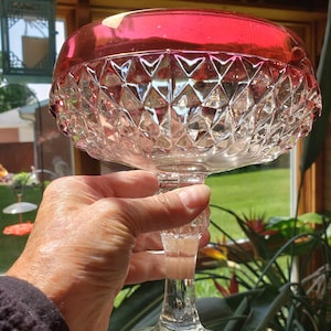 May include: A clear glass bowl with a diamond pattern and a red rim. The bowl is on a clear glass pedestal.