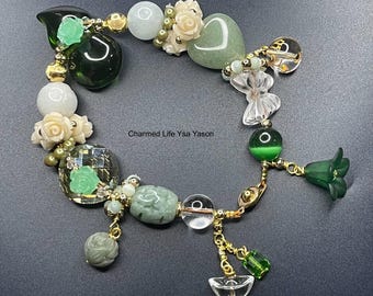 May include: A green and white beaded bracelet with charms, including a heart, a flower, and a butterfly. The bracelet also features a gold clasp and a small green pendant.