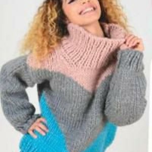 Puede incluir: Un suéter de punto grueso con cuello alto y un diseño de bloques de color en tonos rosa, gris y azul.