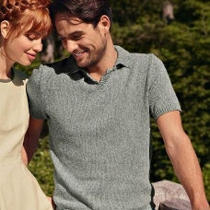 May include: A light green polo shirt with a V-neck collar and short sleeves. The shirt has a textured appearance and is worn by a person. The person is standing outside in front of a green background.