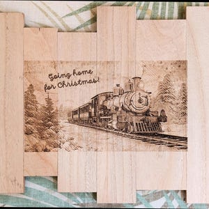 May include: A wooden sign with a laser-engraved image of a train traveling through a snowy forest. The text "Going home for Christmas!" is engraved above the train.