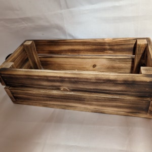 May include: A rustic wooden crate with black metal handles. The crate is made of weathered wood with a dark brown finish.