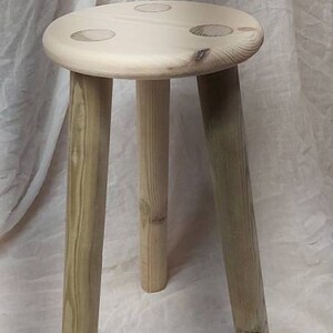 K&ouml;nnte beinhalten: Ein Holzhocker mit drei Beinen und einer runden Oberseite. Der Hocker ist aus Naturholz gefertigt und hat eine hellbraune Farbe.
