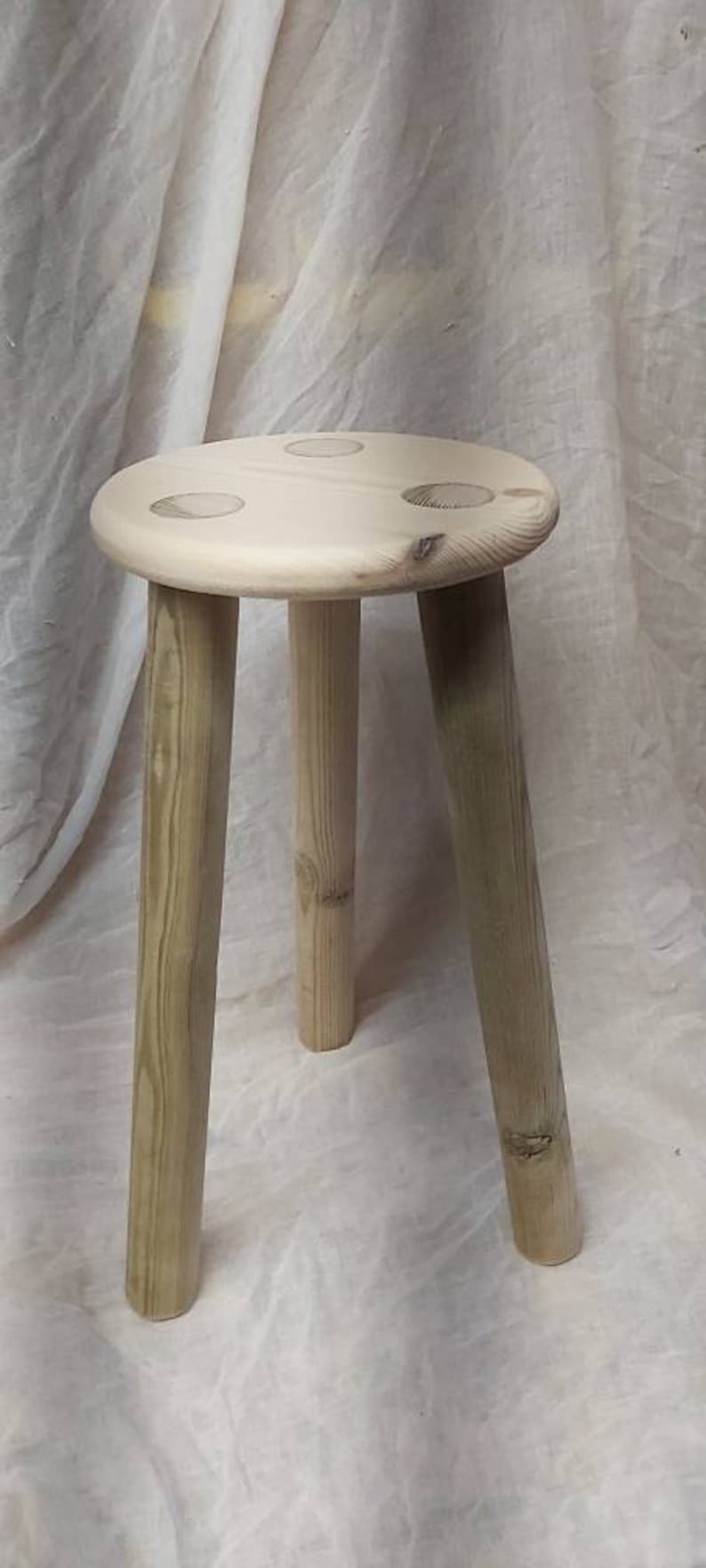 K&ouml;nnte beinhalten: Ein Holzhocker mit drei Beinen und einer runden Oberseite. Der Hocker ist aus Naturholz gefertigt und hat eine hellbraune Farbe.