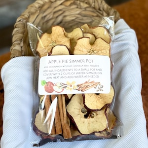 May include: A clear plastic bag filled with dried apple slices, cinnamon sticks, and cloves. The bag has a label that reads "Apple Pie Simmer Pot" and includes instructions for making a simmer pot.