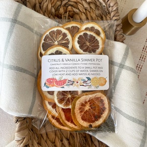 May include: A clear plastic bag filled with dried citrus fruit slices, including grapefruit, lemon, and orange. The bag has a label that reads "Citrus & Vanilla Simmer Pot" and lists the ingredients: grapefruit, vanilla, lemon, thyme, and peppercorn. The label also includes instructions for using the ingredients to make a simmer pot.