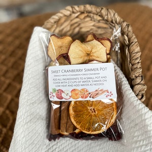 May include: A clear plastic bag filled with dried fruit and spices for making a simmer pot. The bag includes orange slices, apple slices, cinnamon sticks, and cranberries. The label reads "Sweet Cranberry Simmer Pot" and includes instructions for making the simmer pot.
