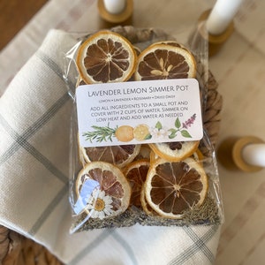 May include: A clear plastic bag filled with dried lemon slices, lavender, rosemary, and dried daisy petals. The bag has a white label with the text "Lavender Lemon Simmer Pot" and instructions for use.