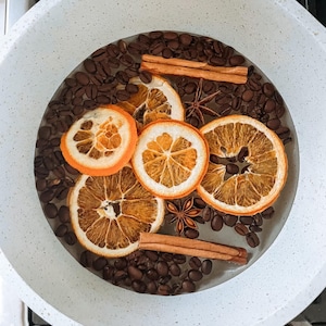 Puede incluir: Una olla blanca llena de granos de caf&eacute;, palitos de canela, an&iacute;s estrellado y rodajas de naranja secas.