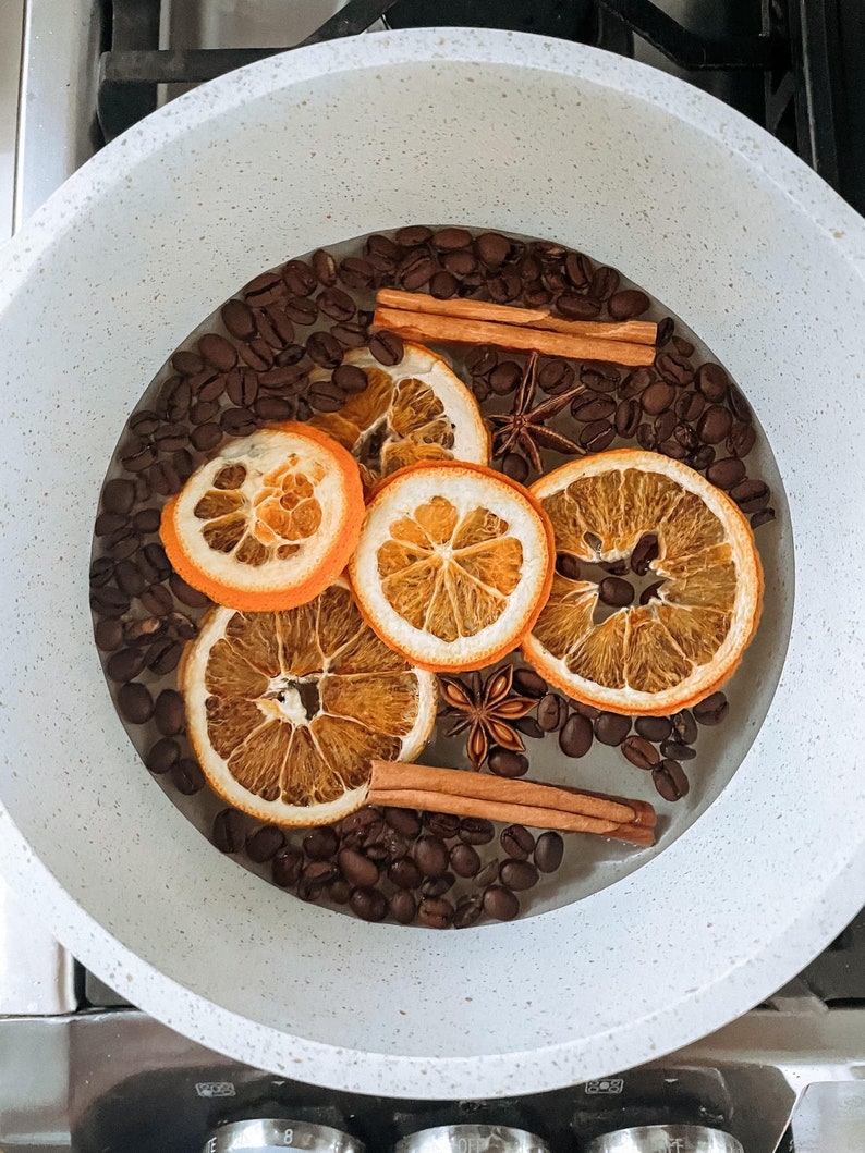 Puede incluir: Una olla blanca llena de granos de caf&eacute;, palitos de canela, an&iacute;s estrellado y rodajas de naranja secas.
