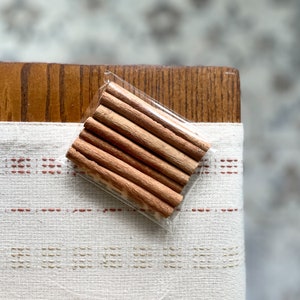 May include: A close-up of a package of cinnamon sticks. The sticks are brown and are wrapped in clear plastic.