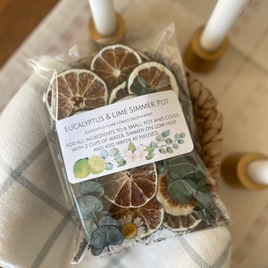 May include: A clear plastic bag filled with dried eucalyptus leaves, lime slices, and daisies. The bag has a white label that reads "Eucalyptus & Lime Simmer Pot" and includes instructions for use.