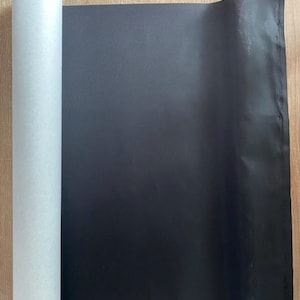 May include: A roll of black fabric with a white backing. The fabric is rolled up and the white backing is visible.