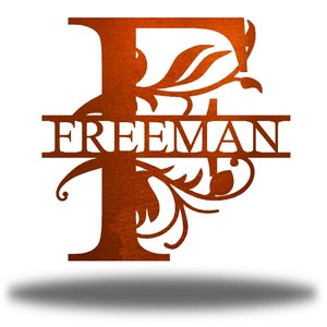 May include: A metal monogram with the letter F and the name "FREEMAN" in a decorative font. The letter F is adorned with intricate floral designs.