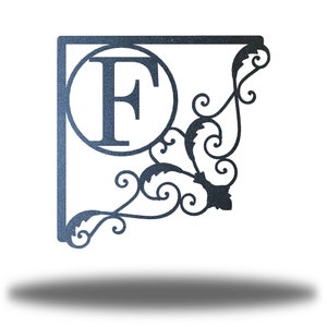 May include: A metal monogram sign featuring the letter "F" within a circle, enclosed by a square frame and an ornate scroll design.