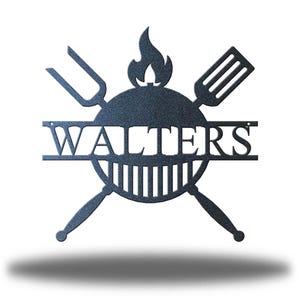 May include: A dark gray metal sign featuring a barbecue grill design. The sign includes a flame, spatula, and fork, with the name "WALTERS" cut out across the center. The sign is designed for outdoor use.