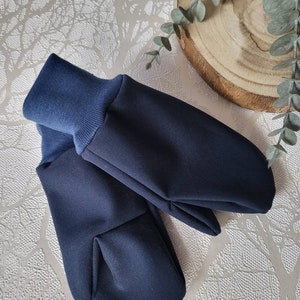 Könnte beinhalten: Ein Paar marineblaue Fäustlinge mit dunkelblauen Rippbündchen. Die Fäustlinge sind aus einem weichen, glatten Stoff gefertigt und sollen die Hände warm halten. Sie liegen auf einer strukturierten, silbernen Oberfläche.